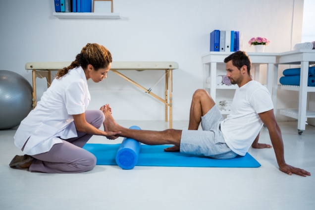 Physiotherapist doing ACL therapy to a man using foam roll in clinic